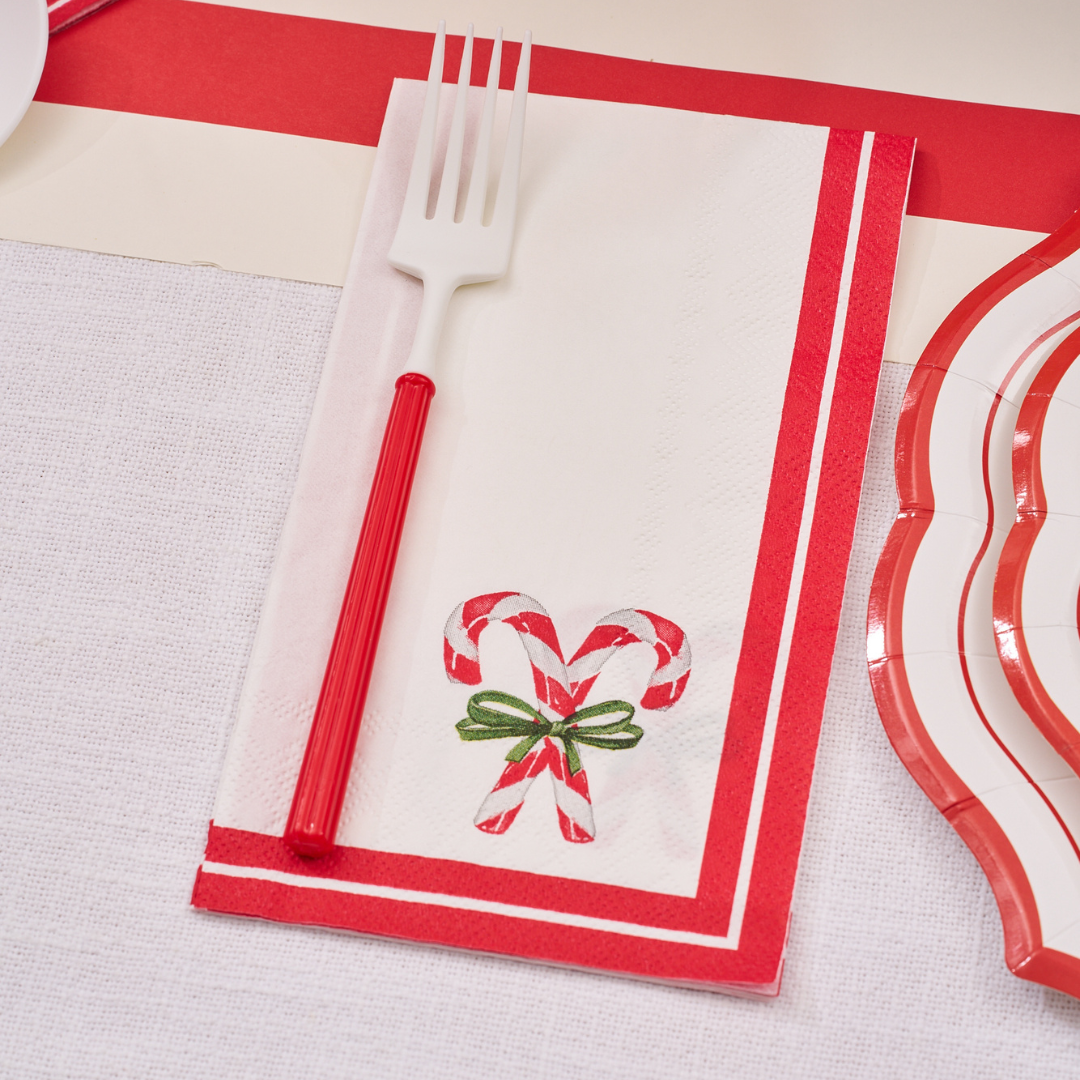 The Merry & Bright: Christmas Table for 16 set features a white napkin with red borders and candy canes tied with a green bow, topped with a red and white plastic fork—ideal for your festive holiday table setting.