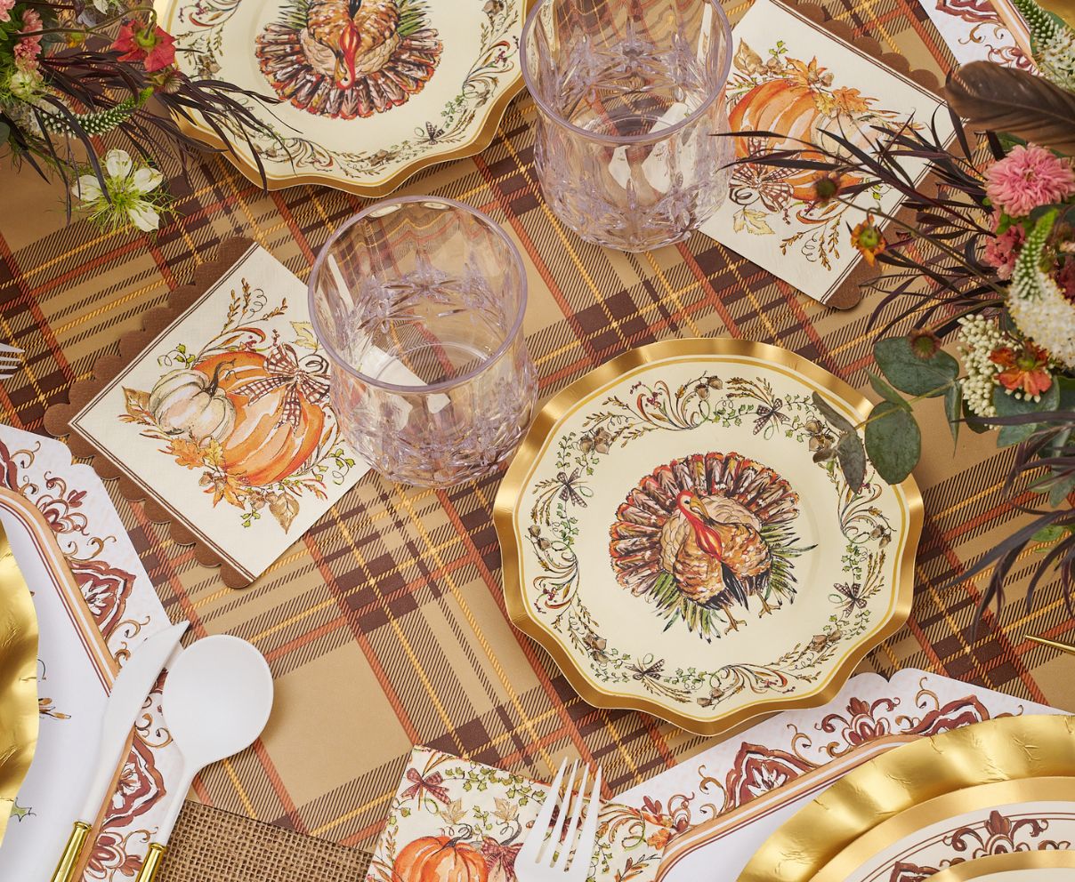 The Turkey & Gourds Table Setting Bundle by Sophistiplate LLC showcases Thanksgiving style with designer disposable plates adorned with turkey motifs, pumpkin-themed napkins, clear glasses, gold-trimmed utensils, and autumn floral centerpieces atop a plaid tablecloth.