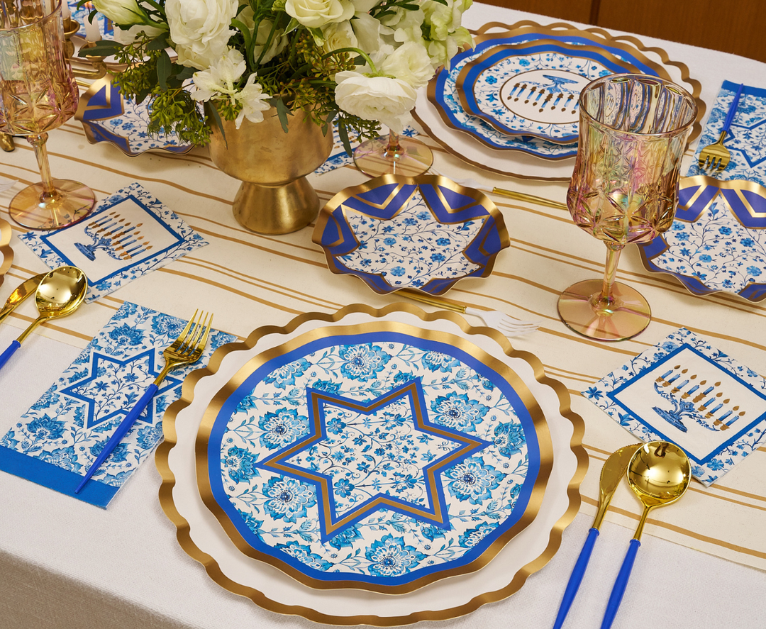 Create a sophisticated Hanukkah celebration with the Sophistiplate Hanukkah Toile Table Setting, featuring blue and gold designer paper plates adorned with Stars of David, gold utensils, menorah napkins, a striking floral centerpiece in a gold vase, and a coordinating striped table runner for an unforgettable festive tablescape.