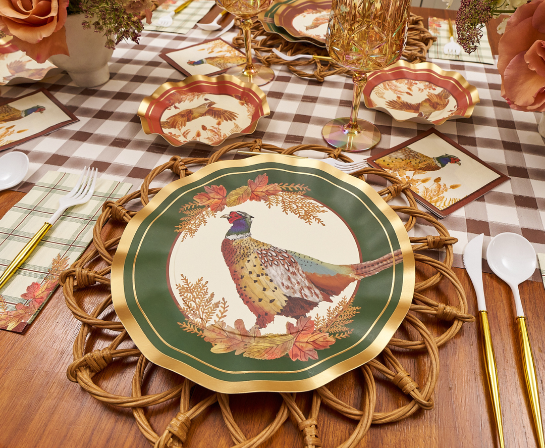 A festive and cozy fall table setting featuring Sophistiplate Woodland Harvest Dinner Plates (8-pack) with a charming pheasant illustration, complemented by autumn leaves, gold-rimmed glasses, gold utensils, and a checkered tablecloth.