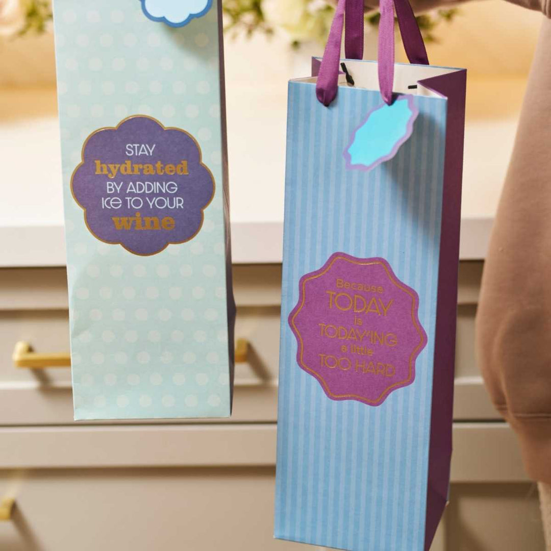 The Drinks On Me Today'ing Wine Bag features two decorative, funny designs with witty sayings—great as reusable wine gift bags or hostess gifts: “Stay hydrated by adding ice to your wine” and “Because today is today and that's too hard.”.