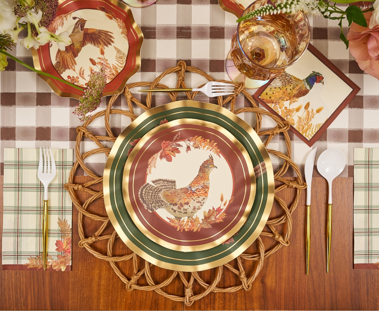 A fall-themed table setting featuring Sophistiplate Woodland Harvest Salad Plates (8pk), napkins and cards adorned with bird illustrations, gold-rimmed utensils, a checkered tablecloth, floral accents, and a woven placemat.