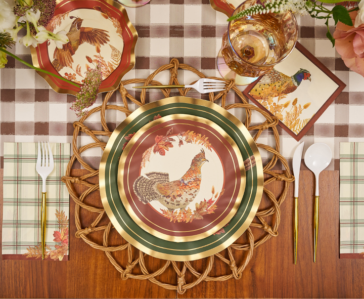 A fall-themed table setting featuring Sophistiplate Woodland Harvest Salad Plates (8pk), napkins and cards adorned with bird illustrations, gold-rimmed utensils, a checkered tablecloth, floral accents, and a woven placemat.