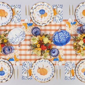 A festive autumn table is set with Sophistiplate Wavy Salad Plate Harvest Blues, blue and white napkins, gold cutlery, blue glasses, floral centerpieces, and decorative pumpkins on an orange checkered table runner.