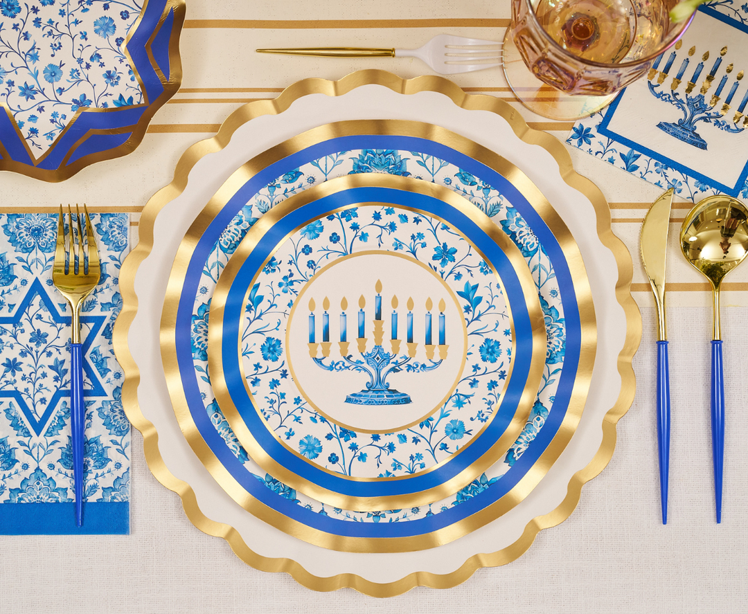 Create a chic and memorable festive tablescape with the Sophistiplate Hanukkah Toile Table Setting—featuring blue, white, and gold designer paper plates adorned with a menorah and blue floral designs, complemented by elegant gold utensils, glassware, festive napkins, and arranged on a cream tablecloth for a truly elegant Hanukkah celebration.