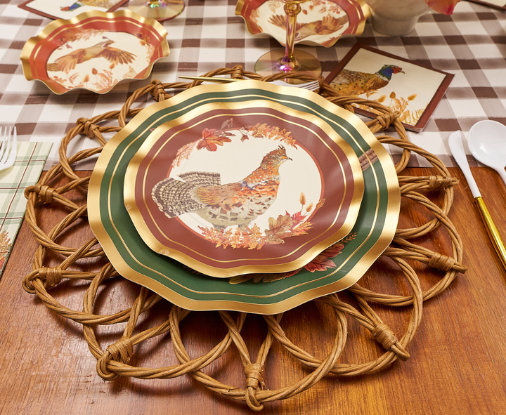 A fall-themed place setting features Sophistiplate Woodland Harvest Salad Plates/8pk with a pheasant design, a woven placemat, gold-trimmed utensils, and a brown-and-white checkered tablecloth.