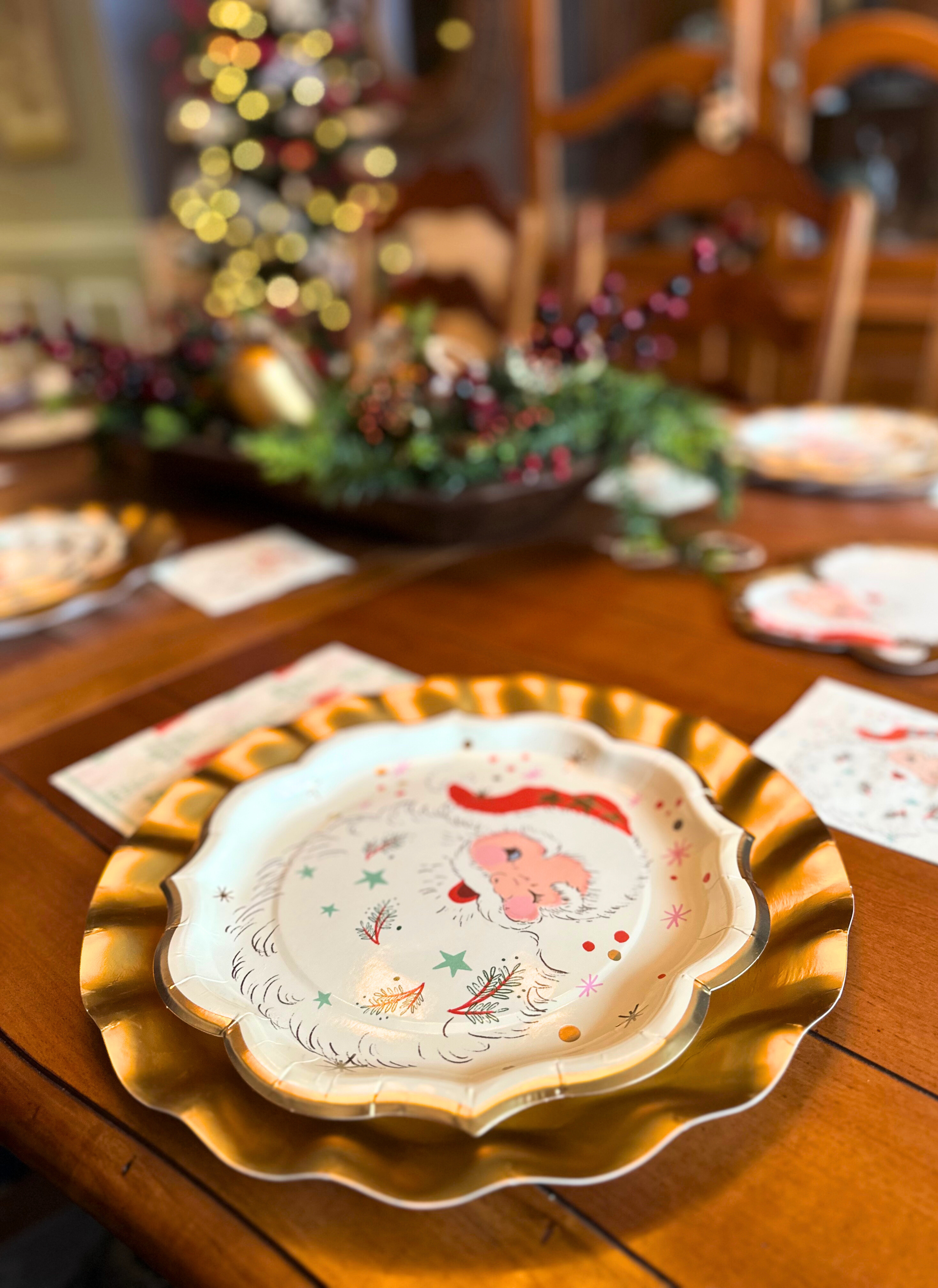 A Vintage Santa: Christmas Table for 16 setting on a wooden table featuring a scalloped plate decorated with a vintage-style Santa Claus illustration and festive accents.