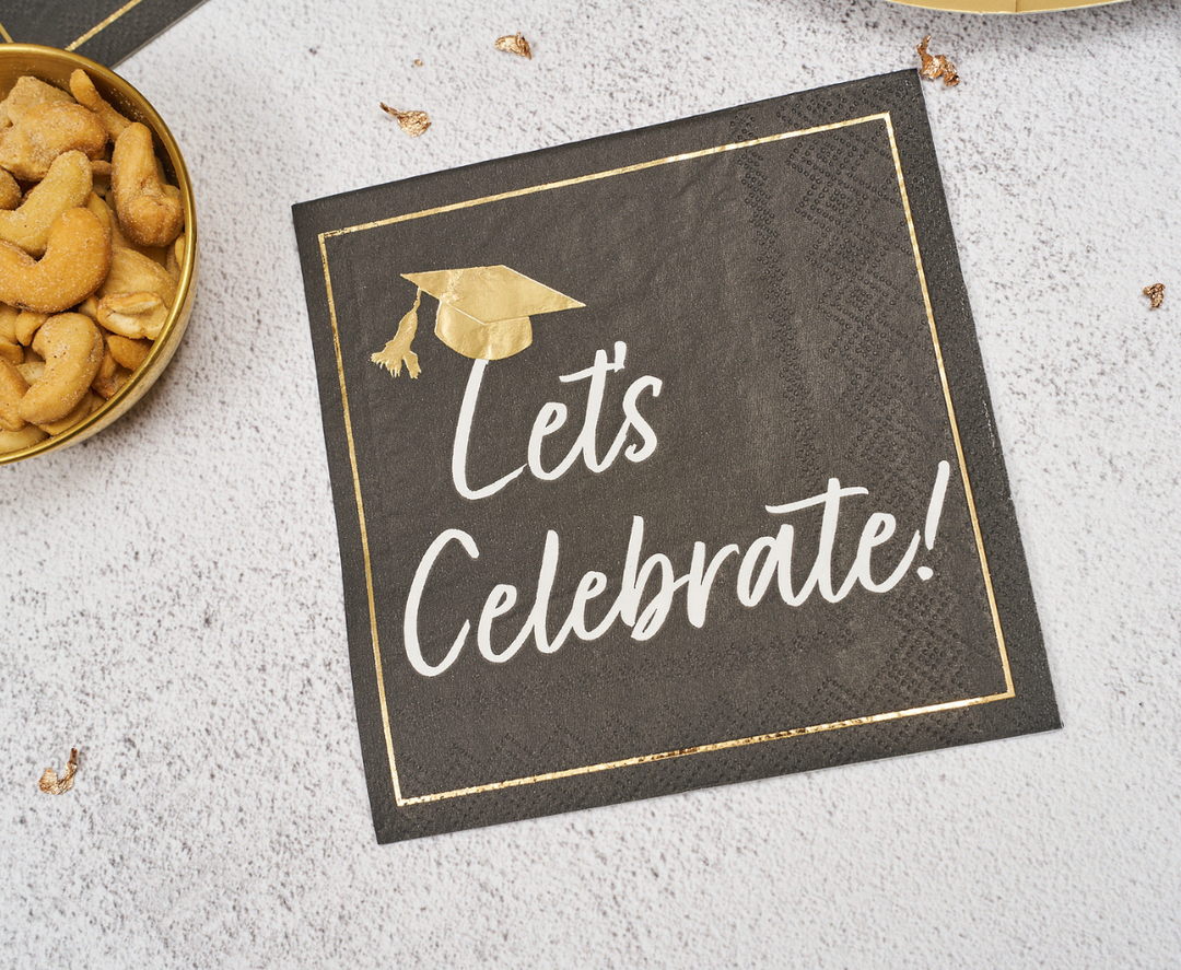 Celebrate your grad with Sophistiplate’s Classic Grad Cocktail Napkins/26pk—black napkins with gold trim and a gold cap graphic, featuring “Let’s Celebrate!” in white script—perfect for your graduation party snacks.