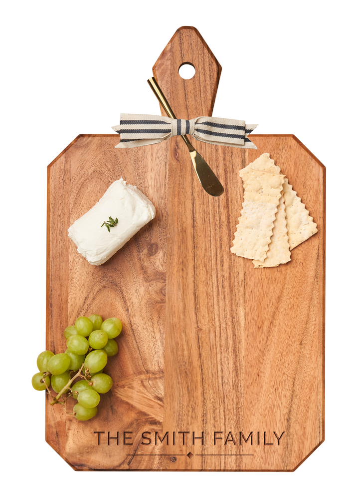 The Maple Acacia Heirloom Board with handle (16x10") displays The Smith Family monogram, topped with soft herbed cheese, green grapes, square crackers, and includes a gold spreader tied with a striped ribbon.