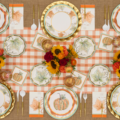 A fall-themed table setting featuring pumpkin and leaf plates, a checkered tablecloth, gold utensils, fall-colored flowers, and autumn leaf napkins is arranged neatly for a festive meal. Bright & Thankful Appetizer/Dessert Bowls by Sophistiplate add a charming touch to the ensemble, perfectly complementing the seasonal décor.