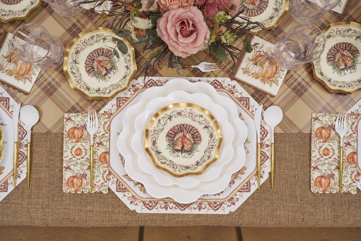 Create a Thanksgiving table setting with the Ivory Harvest Table Setting by Sophistiplate, featuring eco-friendly turkey-themed disposable plates, pumpkin napkins, elegant glassware, and a floral centerpiece with pink roses—all beautifully arranged on a plaid tablecloth and rustic burlap runner.