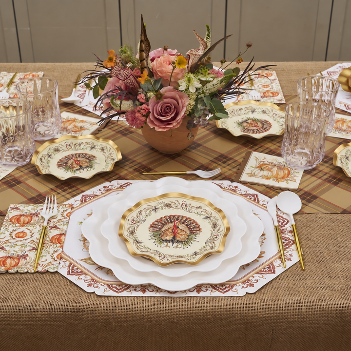 Create an inviting autumn tablescape with the Ivory Harvest Table Setting by Sophistiplate, featuring compostable plates adorned with a charming turkey motif, clear glasses, festive napkins, and gold flatware. Pink and orange floral centerpieces rest atop a plaid and burlap tablecloth for added warmth. This eco-friendly Thanksgiving tableware beautifully blends style and sustainability—perfect for your holiday gatherings.