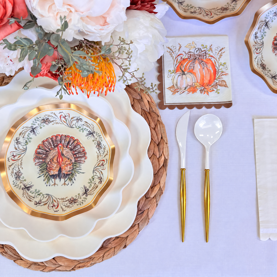Set a festive Thanksgiving table with Ivory Harvest: Thanksgiving Table for 16 by Sophistiplate LLC, featuring disposable plates, gold cutlery, pumpkin napkins, and a floral centerpiece on a woven placemat.