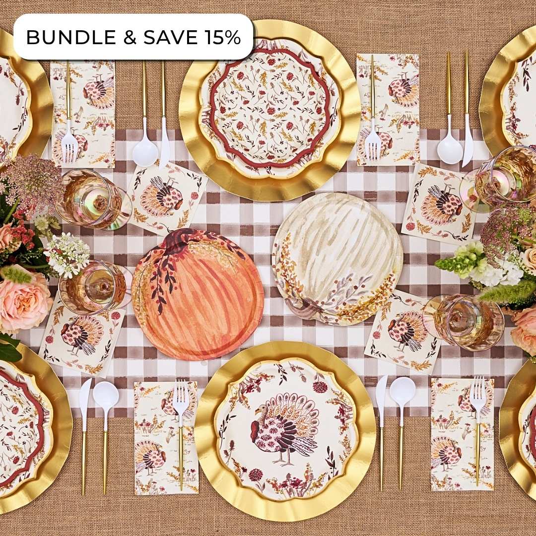 Overhead view of an Amber Harvest: Thanksgiving Table for 16 setting featuring heavy duty paper plates with turkey and pumpkin motifs, gold-rimmed charger plates, and floral napkins on a checkered runner.