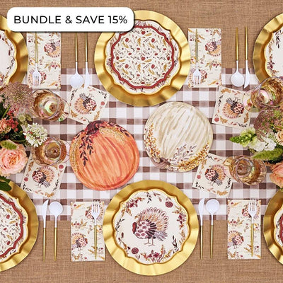 Overhead view of an Amber Harvest: Thanksgiving Table for 16 setting featuring heavy duty paper plates with turkey and pumpkin motifs, gold-rimmed charger plates, and floral napkins on a checkered runner.