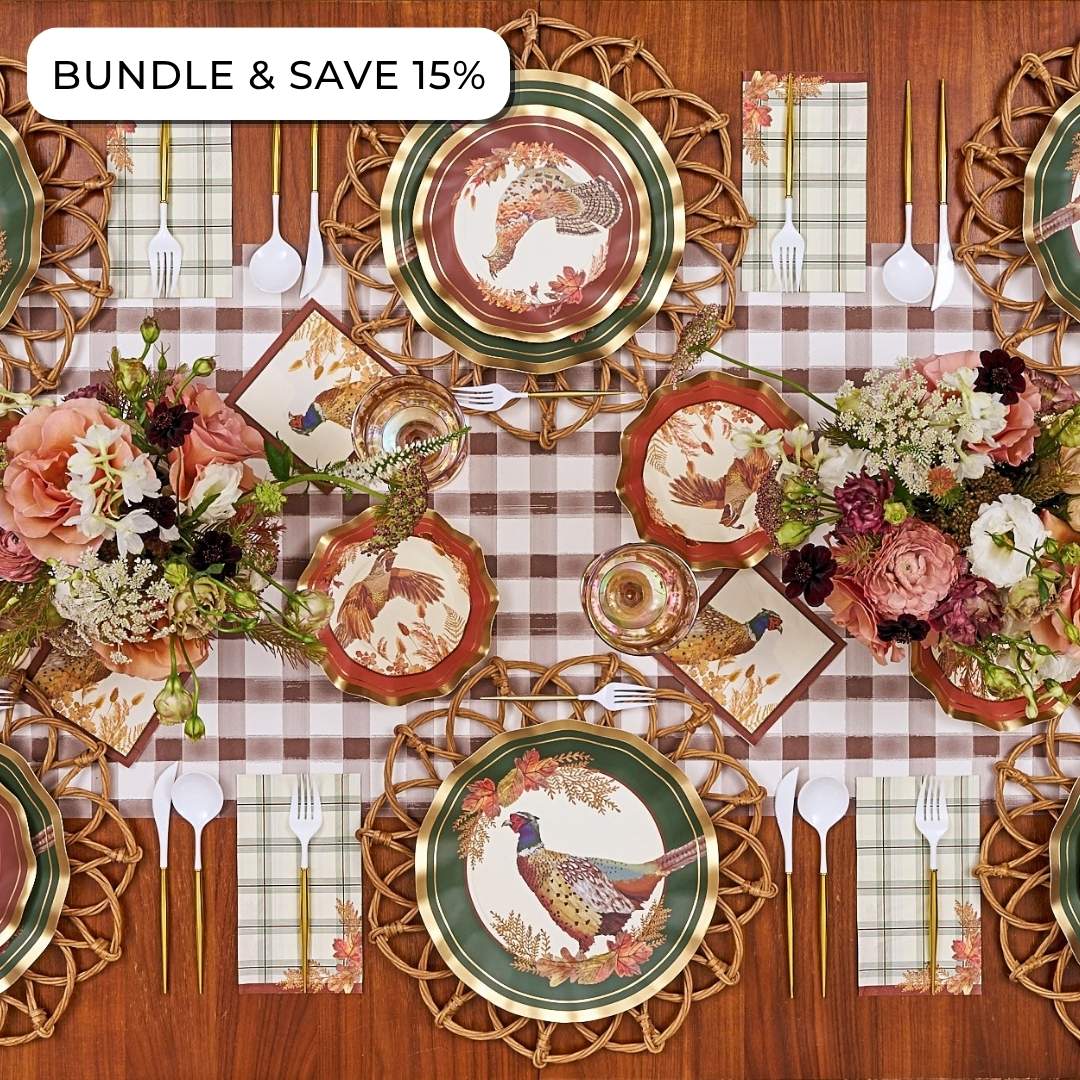 A Woodland Harvest: Thanksgiving Table for 16 set with pheasant and autumn leaf paper plates, napkins, woven chargers, gold-handled cutlery, and floral centerpieces on a brown plaid tablecloth.
