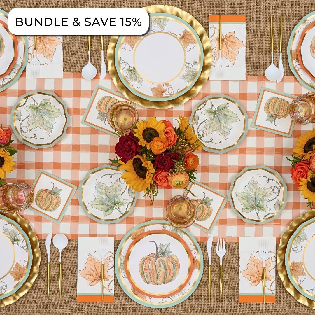 Overhead view of a Bright & Thankful: Thanksgiving Table for 16 set with autumn-themed paper plates, gold-rimmed chargers, gold cutlery, and a centerpiece of sunflowers and roses.