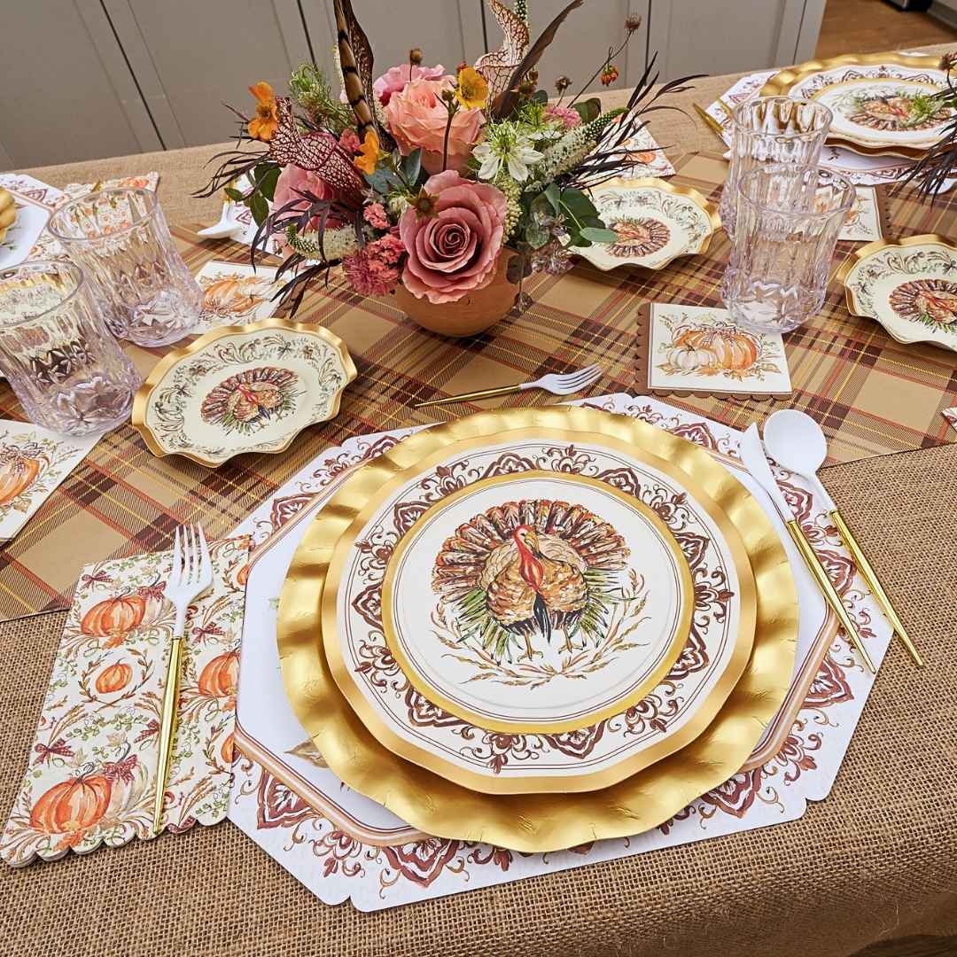 A Turkey & Gourds: Thanksgiving Table for 16 set featuring heavy duty paper plates with turkey and gourd illustrations, gold-rimmed chargers, floral napkins, and a central flower arrangement.