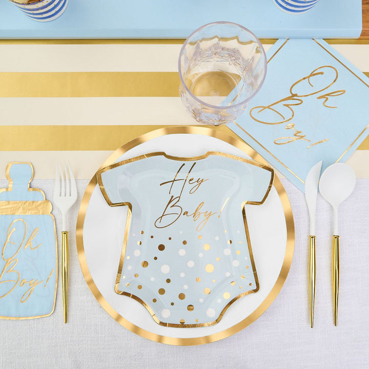 The Hey Baby Blue Table Setting by Sophistiplate LLC features a onesie-shaped plate with "Hey Baby!", gold-rimmed plate, blue "Oh Boy!" napkins, gold utensils, plastic cup, and gold-white striped placemat.