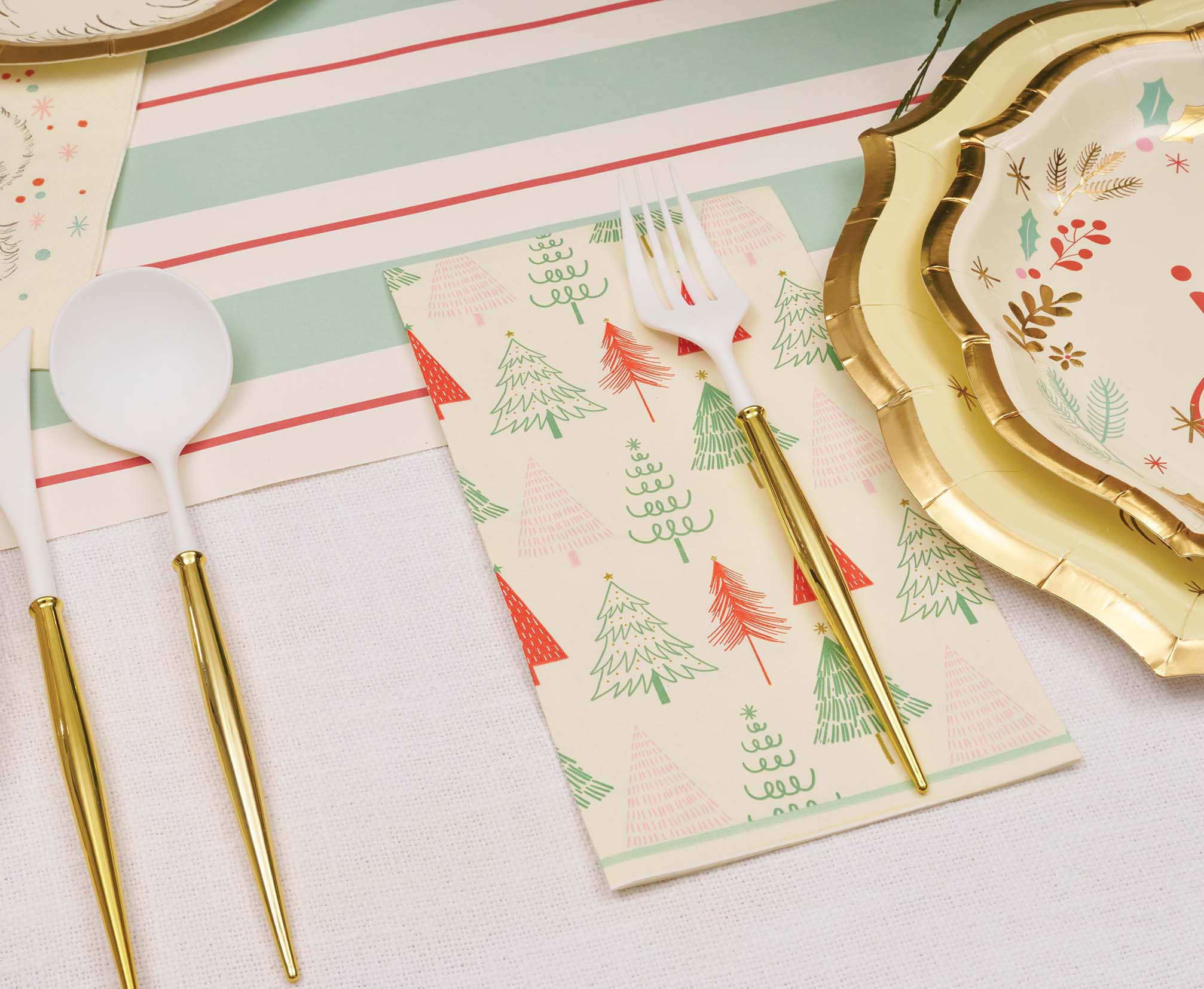 Create a festive table with the Sophistiplate Vintage Santa Table Setting, featuring gold-rimmed designer disposable plates, gold and white cutlery, and a napkin adorned with red and green Christmas trees on a striped runner.
