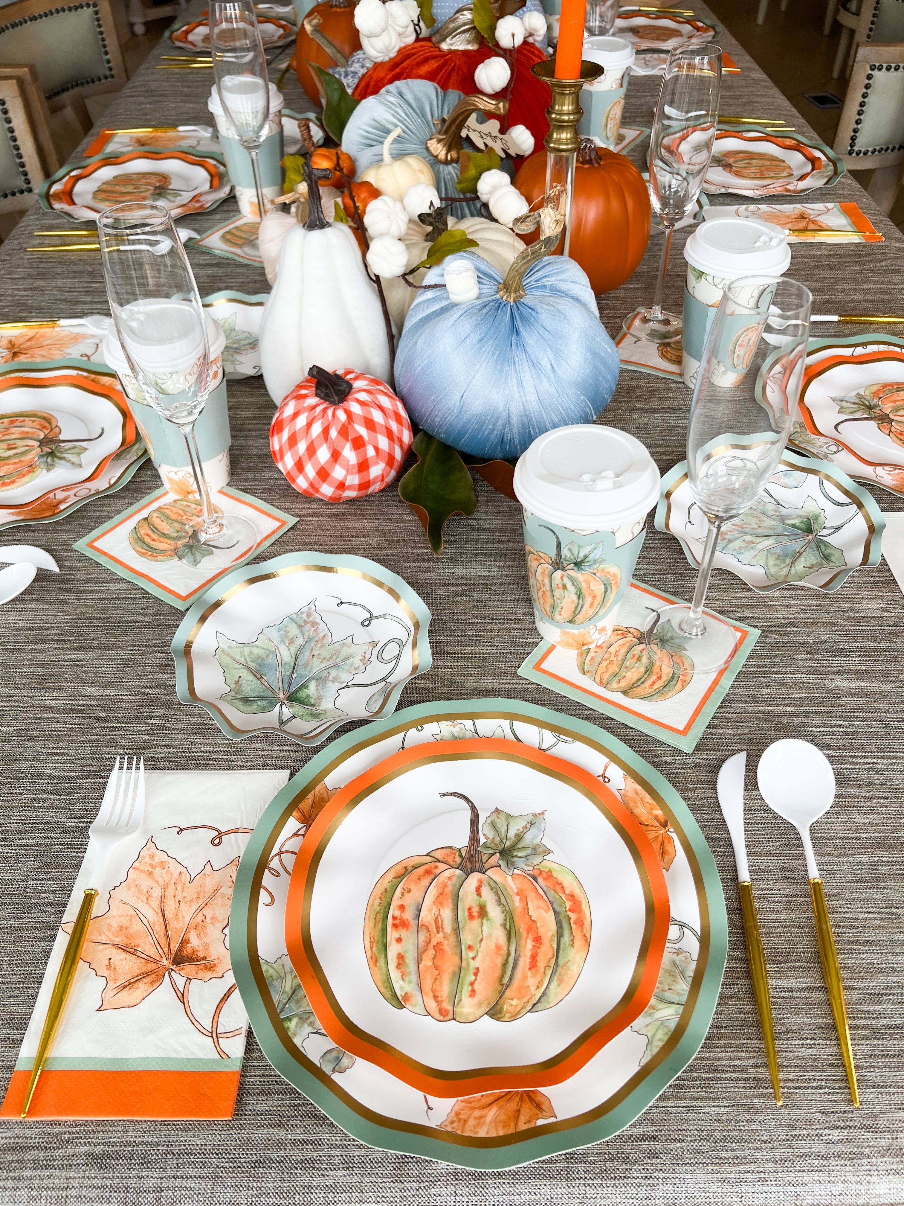 The Bright & Thankful Table Setting by Sophistiplate features autumn-inspired plates, leaf napkins, disposable cups, and orange, white, and blue gourds as a centerpiece for a festive tablescape with coordinated flatware and glasses.