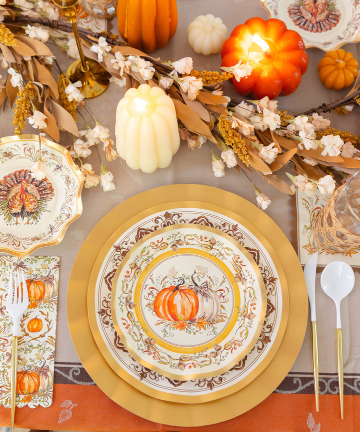 Create a warm and inviting Thanksgiving tablescape with the Turkey & Gourds Table Setting by Sophistiplate, featuring pumpkin-themed designer paper plates, gold chargers, faux pumpkins, candles, a floral garland, and vintage turkey napkins. White and gold flatware is arranged beside each place setting atop an orange tablecloth for a festive autumn look.