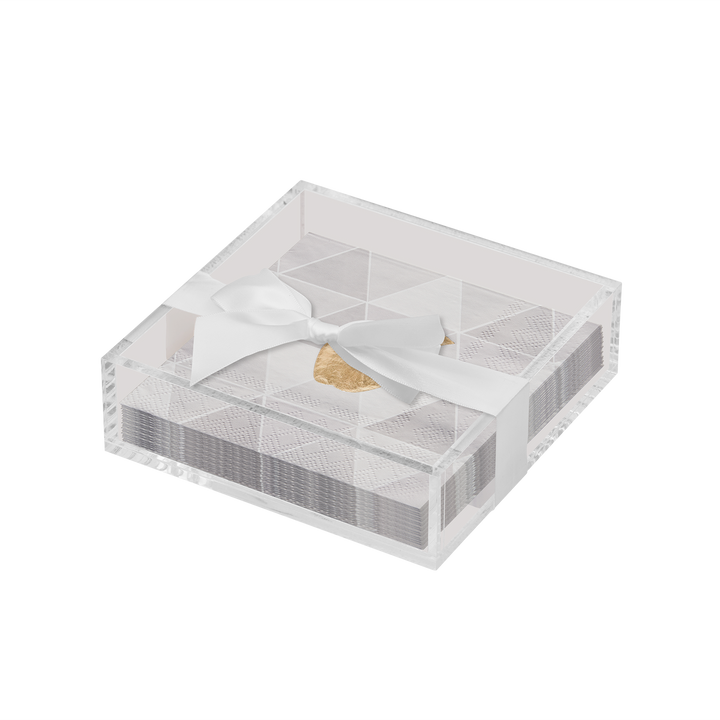 The Sophistiplate Golden Apple Cocktail Napkins with Acrylic Tray features stylish white and silver napkins neatly arranged in a clear acrylic tray, elegantly finished with a white ribbon bow and a gold accent—an exquisite addition to any modern tabletop décor.