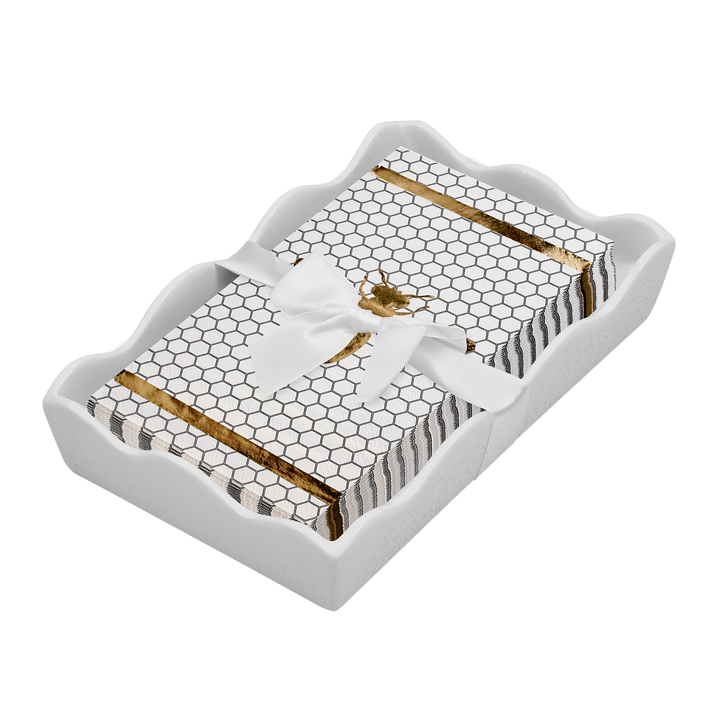 The Sophistiplate Honeybee Guest Towels with Ceramic Tray features a decorative white ceramic tray holding bee-themed guest towels adorned with a honeycomb pattern, gold stripes, and a gold bee design, all elegantly tied with a white ribbon.