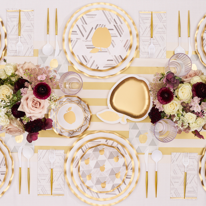 Transform your Rosh Hashanah table with the Sophistiplate Golden Apple Table Setting, featuring elegant gold-striped disposable plates, gold cutlery, and white utensils. Each place is adorned with Sophistiplate’s signature Golden Apple plates and matching glasses atop a striped tablecloth, complemented by floral centerpieces and geometric patterns for a festive touch.