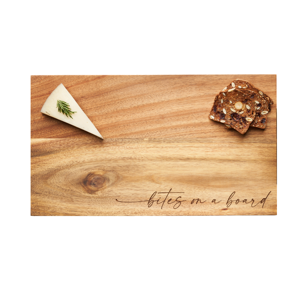 Showcasing Maple’s Modern Acacia Rectangle serving board (14 x 8″) in “Bites on a Board” script, this beautifully crafted acacia wood piece is styled with a wedge of cheese topped with fresh herbs on the left and a small stack of seeded crackers on the right—perfectly capturing the inviting spirit of modern charcuterie.