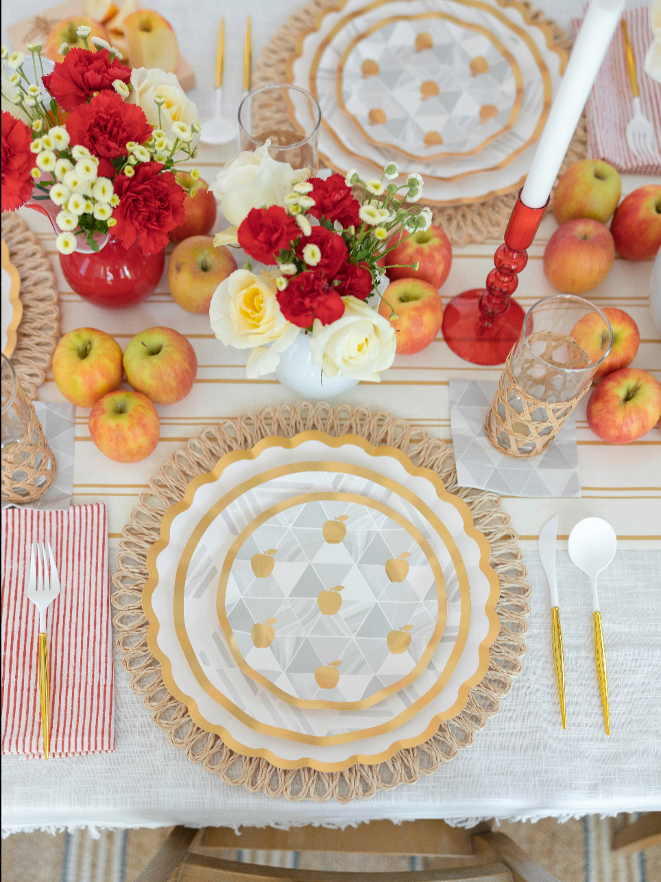 Set a festive and colorful Rosh Hashanah table with the Sophistiplate LLC “Rosh Tablescape for 16 Guests: Golden Apple” set, featuring apple-themed heavy duty paper plates, red and white floral arrangements in vases, scattered apples atop a striped cloth, gold utensils, checkered glasses, and red-striped napkins for a celebratory holiday setting.