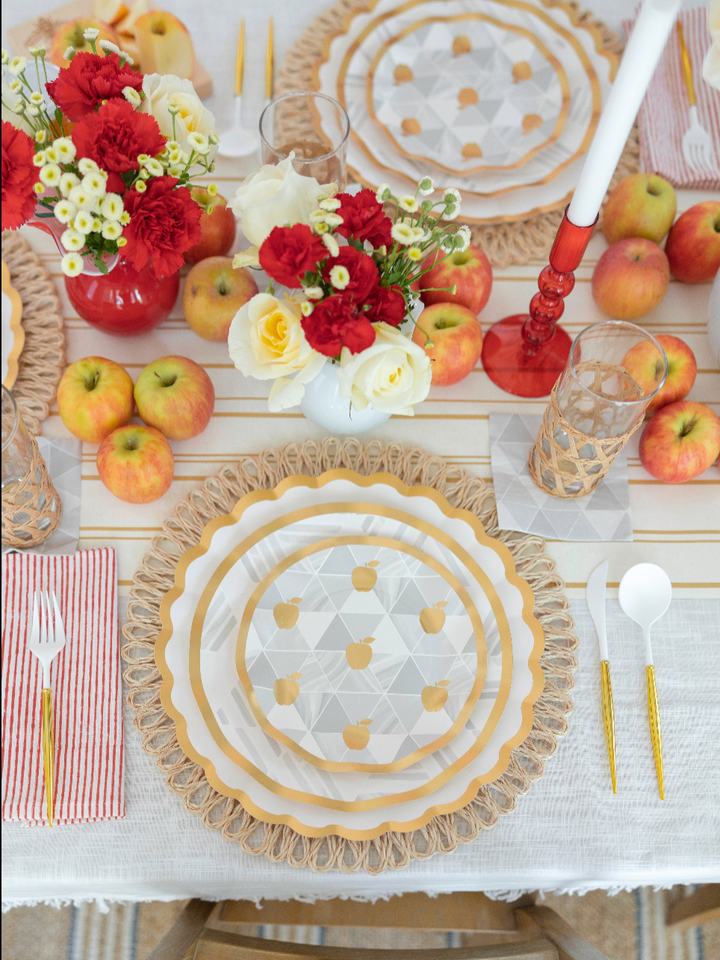 Set a festive and colorful Rosh Hashanah table with the Sophistiplate LLC “Rosh Tablescape for 16 Guests: Golden Apple” set, featuring apple-themed heavy duty paper plates, red and white floral arrangements in vases, scattered apples atop a striped cloth, gold utensils, checkered glasses, and red-striped napkins for a celebratory holiday setting.