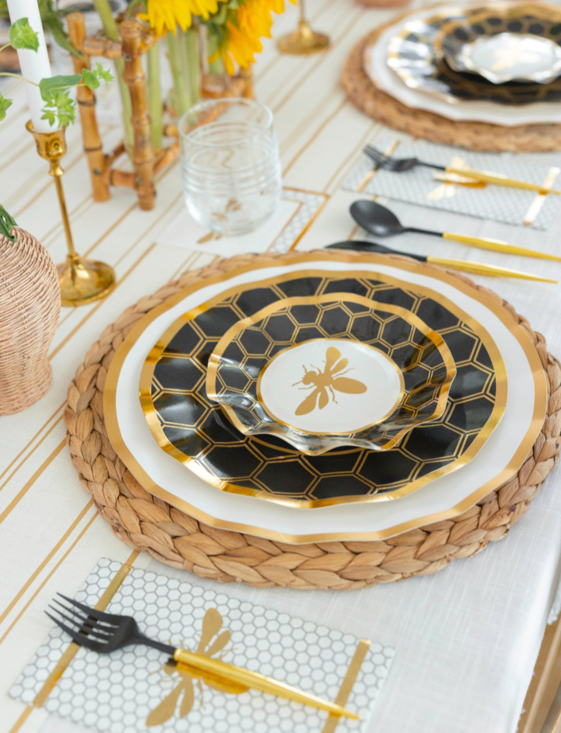 Create an elegant Rosh Hashanah tablescape with the Sophistiplate Rosh Tablescape for 16 Guests: Honeybee set. These black and gold disposable party plates feature a striking honeycomb pattern and a charming bee motif at the center, offering both beauty and durability for your celebration. Paired with gold utensils, woven placemats, clear glassware, sunflower accents, and arranged on a crisp white tablecloth, this set brings convenience and sophistication to your festive gathering.