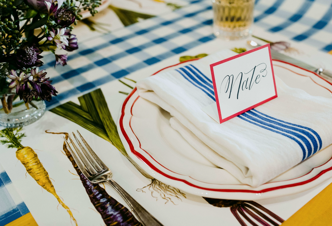 A Red Frame Place Card/12ct reading Mate sits on a folded white napkin atop a plate.