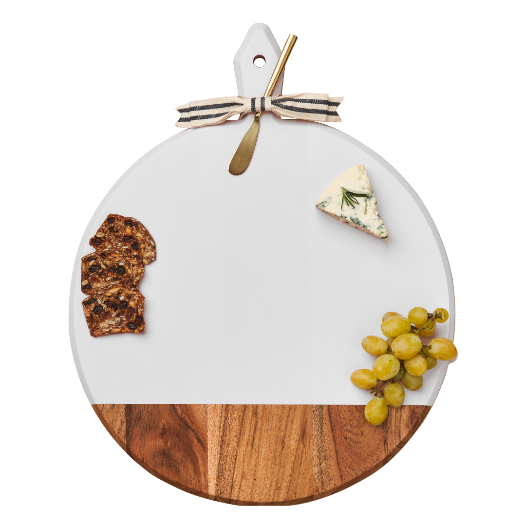 The Maple Acacia Heirloom Board Round in White (20 x 16", customizable) features a white top half, wood bottom, and can be styled with green grapes, blue cheese, crackers, and a small cheese knife tied with a striped ribbon.