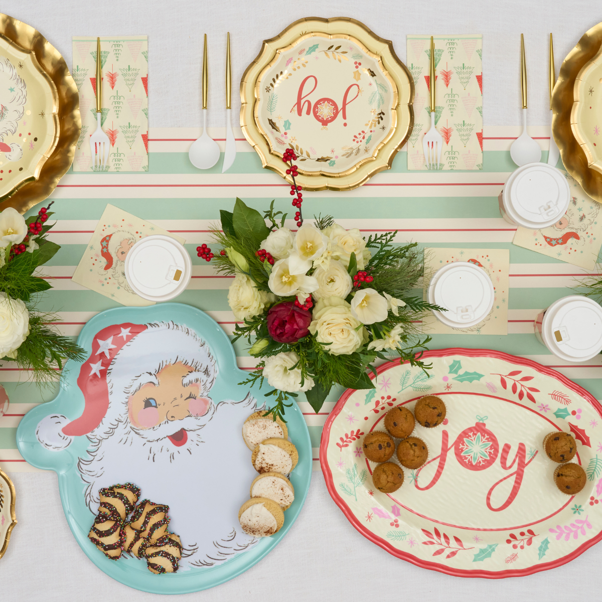 Create a festive tablescape with the Sophistiplate Vintage Santa Table Setting, featuring gold and pastel disposable plates, holiday napkins and cutlery, a floral centerpiece, cookies on themed platters, and cups with lids.