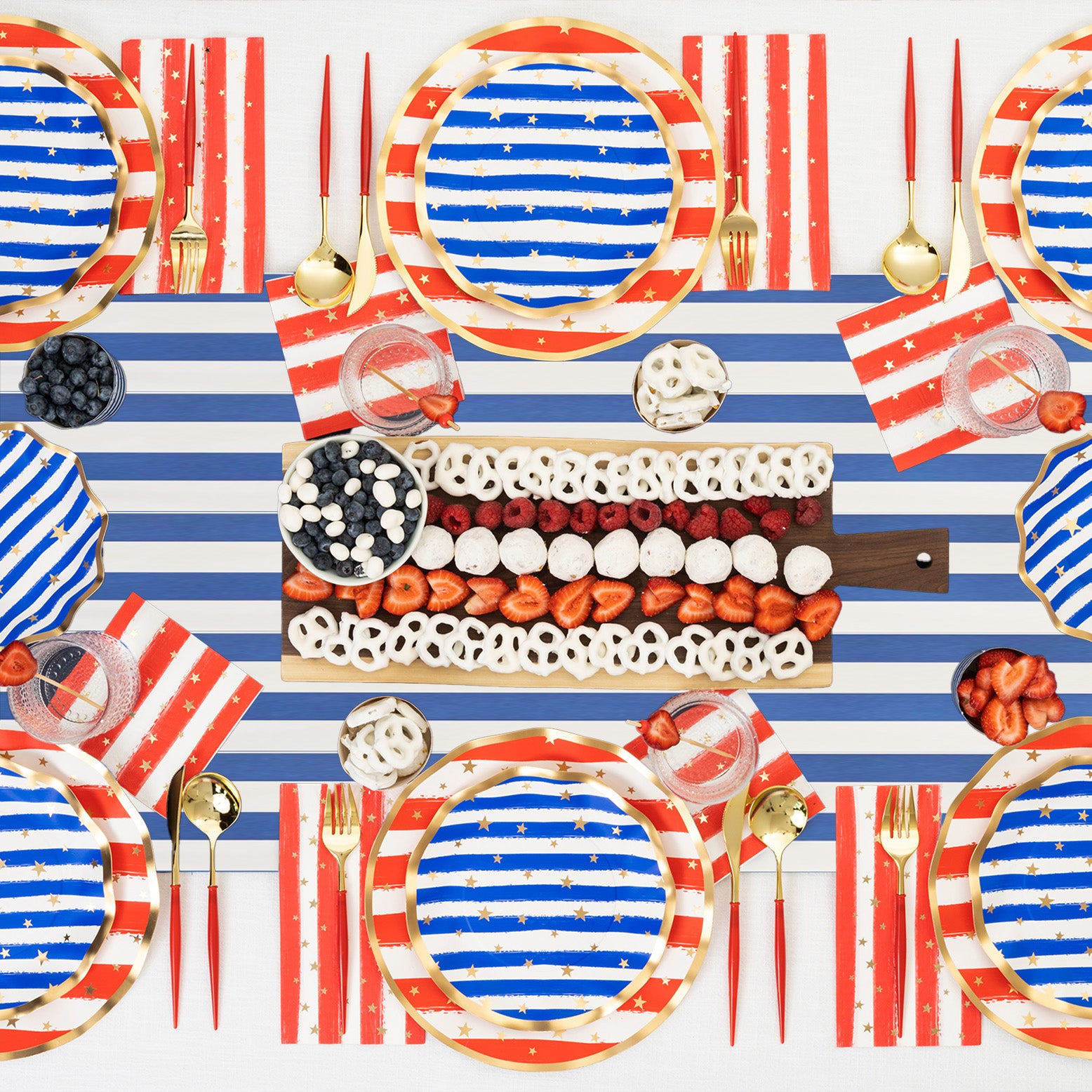 A festive table setting with red, white, and blue plates, napkins, and a striped table runner. The centerpiece is a platter with berries and white treats arranged to resemble the American flag.