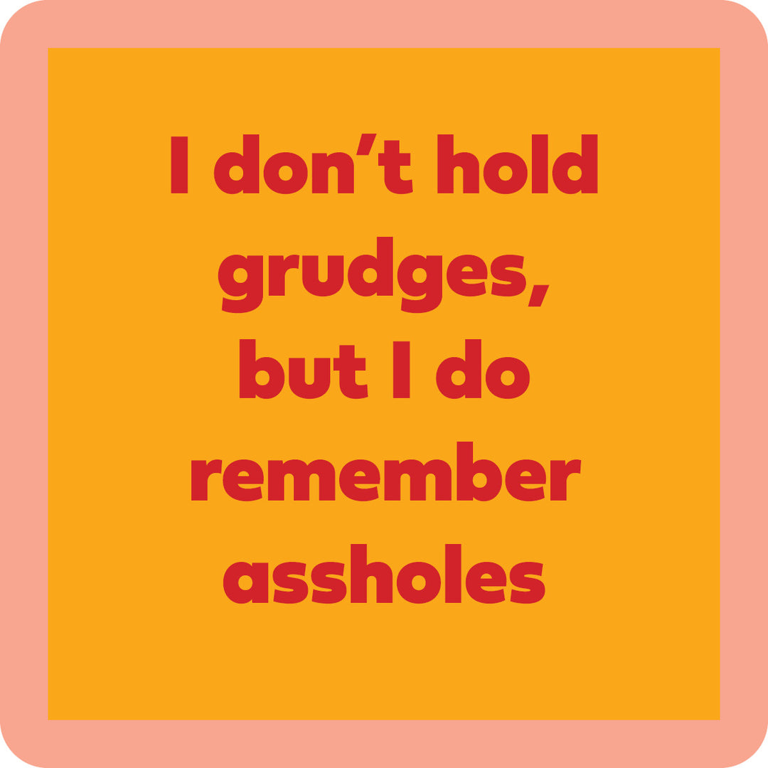 The Grudges Coaster by Drinks On Me features bold red text—“I don’t hold grudges, but I do remember assholes”—on an orange background with a peach border. Great for funny drink coaster designs or quirky bar cart accessories.
