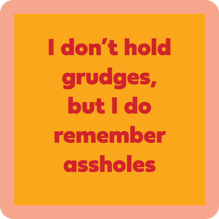 The Grudges Coaster by Drinks On Me features bold red text—“I don’t hold grudges, but I do remember assholes”—on an orange background with a peach border. Great for funny drink coaster designs or quirky bar cart accessories.