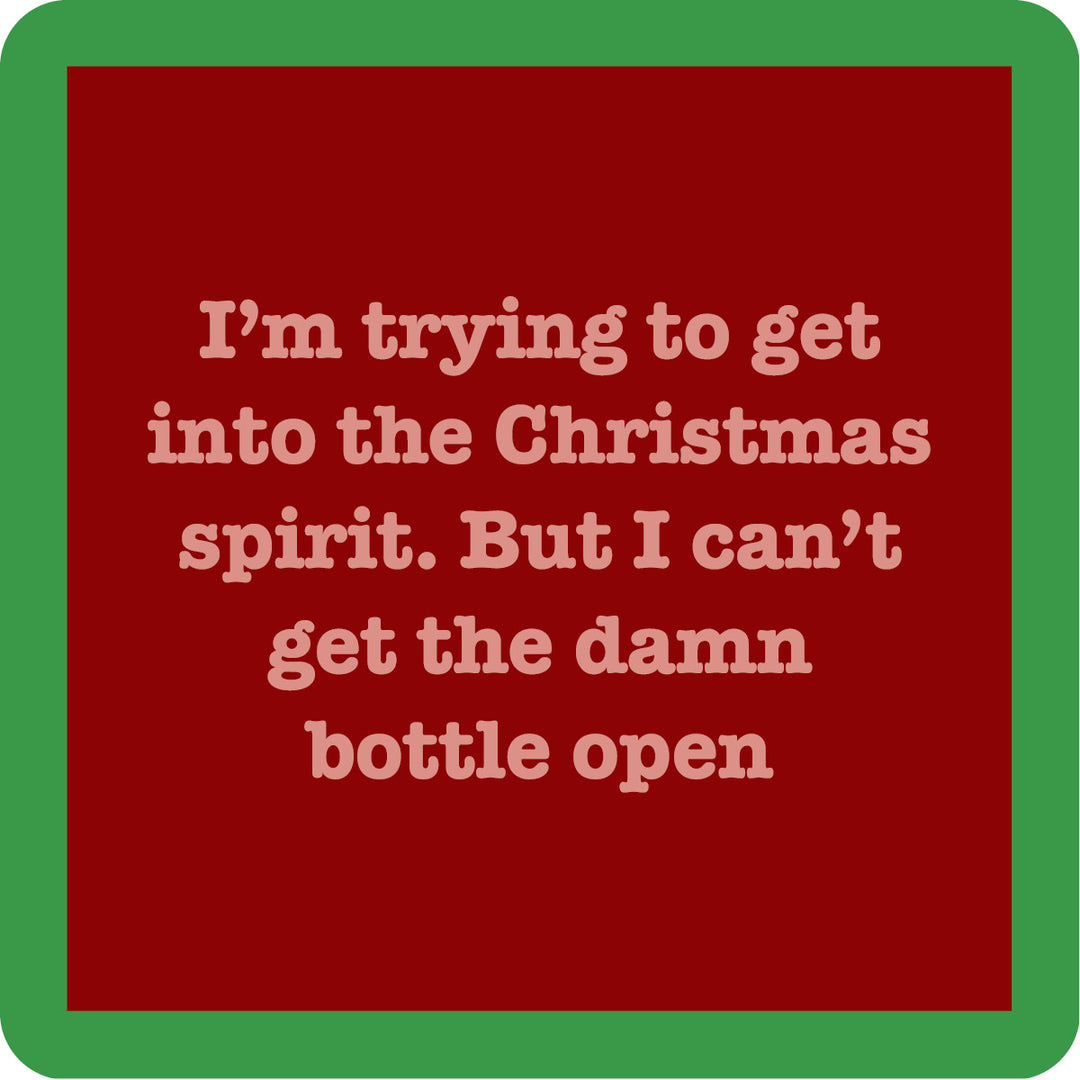 A red square coaster from Drinks On Me features beige text: “I’m trying to get into the Christmas spirit. But I can’t get the damn bottle open”—a funny Bottle Open Coaster for your bar cart or as a cheerful drink accessory.