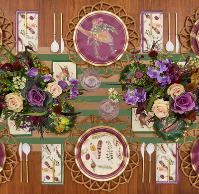 The Feather Grove Table Setting by Sophistiplate features elegant purple and gold disposable plates, botanical napkins, gold utensils, and white-handled cutlery on a wooden table with floral accents and a green-striped runner for a stunning fall look.