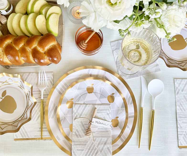 A festive Rosh Hashanah table is set with the Sophistiplate LLC “Rosh Tablescape for 16 Guests: Golden Apple,” featuring elegant designer disposable plates adorned with golden apple motifs, complemented by honey, apples, challah bread, fresh flowers, and gold utensils—all beautifully arranged for a joyous celebration.