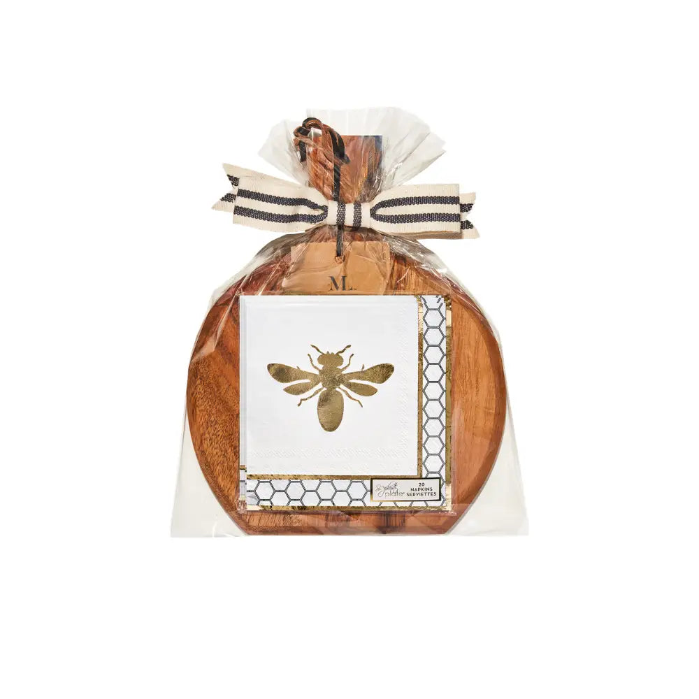 A 9.75″ x 8″ Honeybee Board Gift Kit by Sophistiplate, featuring a round acacia wood charcuterie serving board wrapped in clear plastic and tied with a striped ribbon, with a card showcasing a gold bee illustration and honeycomb pattern attached to the front.