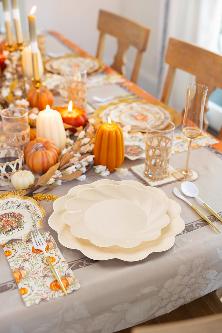 An inviting autumn table display—the Ivory Harvest Table Setting by Sophistiplate—showcases eco-friendly plates surrounded by candles, small pumpkins, glasses, utensils, and floral arrangements on a patterned tablecloth, all beautifully arranged and ready for your festive meal.