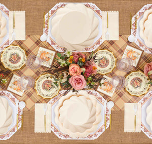 An overhead view of a decorated table set with Sophistiplate LLC’s Ivory Harvest: Thanksgiving Table for 16, featuring floral centerpieces, eco-friendly plates, gold cutlery, plaid tablecloth, and themed napkins.