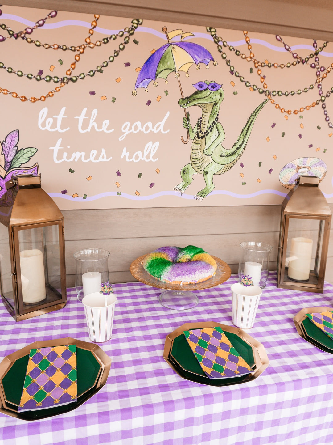 The Sophistiplate Let’s Mardi Table Setting offers a Mardi Gras-inspired tablescape-in-a-box, complete with green and gold designer disposable plates, cupcakes, king cake, candles, and lanterns. An included wall sign features an alligator with beads and an umbrella alongside the phrase “let the good times roll.”.
