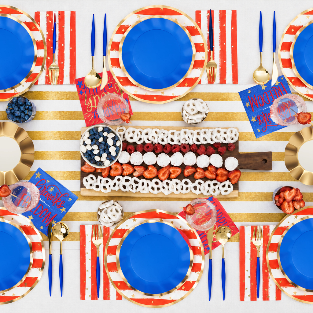 Celebrate with the 4th of July Table for 16+ by Sophistiplate LLC—featuring patriotic confetti, blue party plates, gold utensils, red, white & blue napkins, and a centerpiece with festive striped desserts.