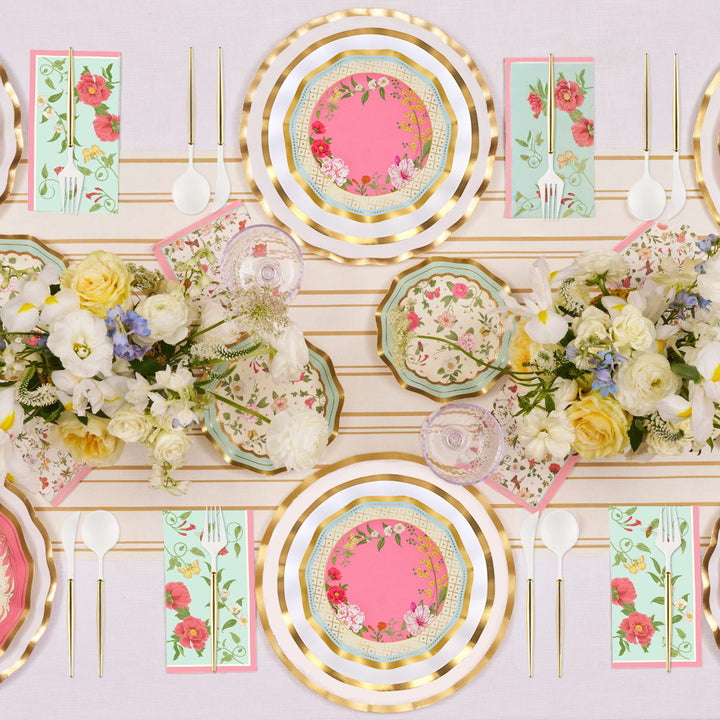 Elevate your event with the Ivory Rococo Table Setting by Sophistiplate—designer disposable plates with gold rims, paired with floral napkins, white cutlery, and lush flower centerpieces showcasing white and yellow blooms atop a light tablecloth—offering a sophisticated party-in-a-box experience.