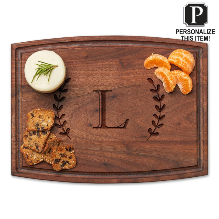 The Maple Personalized Walnut Wood Cutting + Cheeseboard 12 x 9" features an engraved letter L with decorative branches, displaying cheese with herbs, crackers, and clementine segments. A “Personalize this item!” label is shown at the top right.