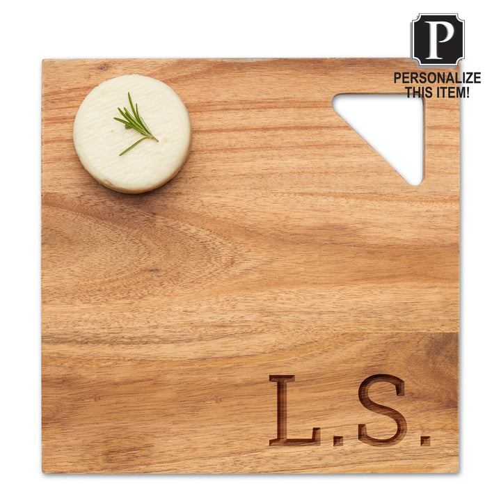 A 12" Acacia Modern Geo Square board by Maple features a triangular cutout handle, engraved initials “L.S.” at the bottom right, paired with a round cheese and rosemary sprig. Tag: Personalize this personalized charcuterie board!.